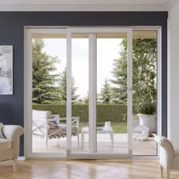 Eleganckie, trzyskrzydłowe, przesuwne drzwi balkonowe z białymi ramami, otwierające widok na patio z zielenią, widoczne z wnętrza salonu z książkami i nowoczesnym obrazem.