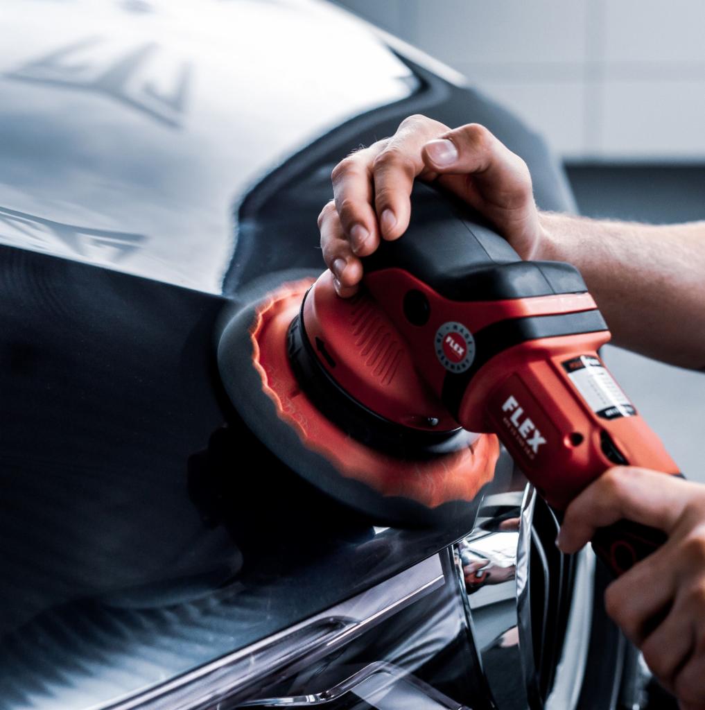 Polerowanie czarnego lakieru samochodu profesjonalną polerką Flex z pomarańczową gąbką polerską.