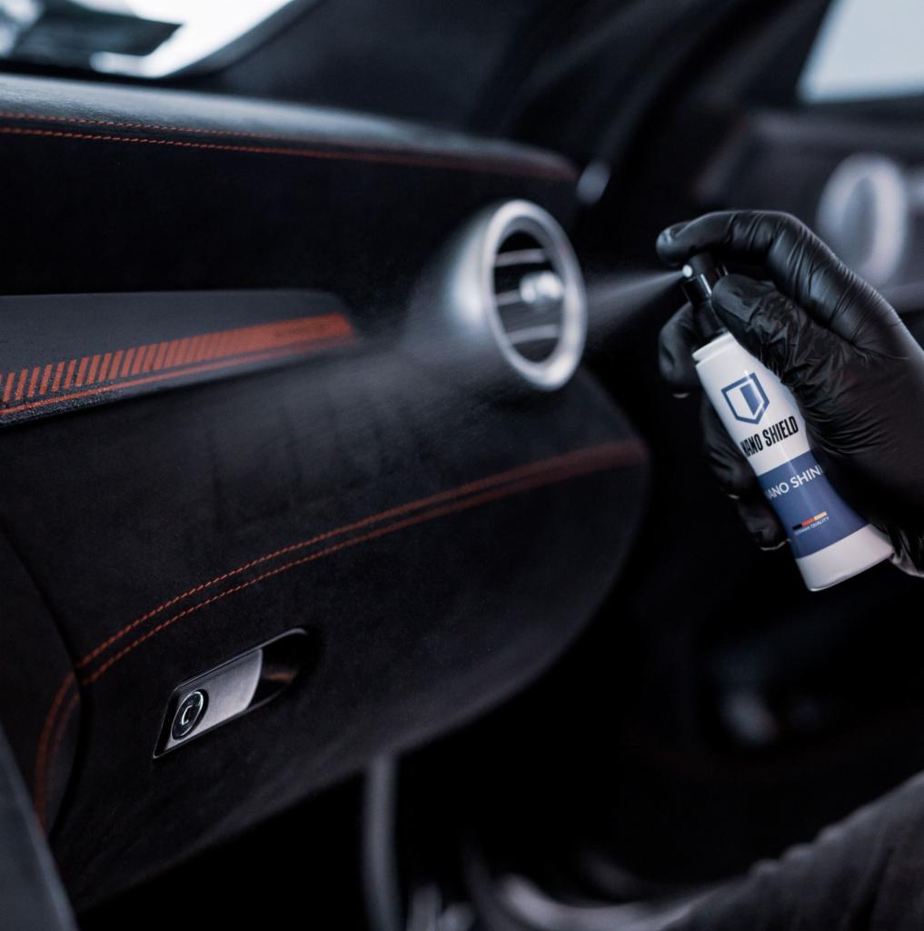 Czyszczenie welurowej deski rozdzielczej w samochodzie za pomocą preparatu Nano Shield, aplikowanego przez osobę w czarnych rękawiczkach.