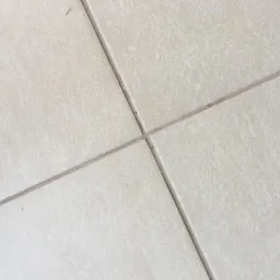 Beżowe płytki podłogowe ułożone ukośnie, widoczne fugi z delikatnym zabrudzeniem w miejscu skrzyżowania.