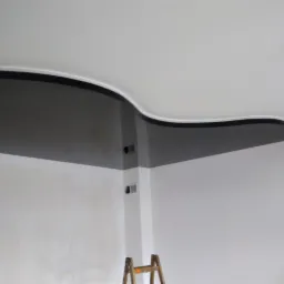 Wykończony fragment wnętrza z pomalowaną na szaro, falistą dekoracją pod sufitem, widoczna drabina malarska.