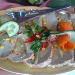 Półmisek z plastrami mięsa w galarecie, udekorowany ogórkiem, kukurydzą, papryką i natką pietruszki, z widelcem i nożem na wierzchu