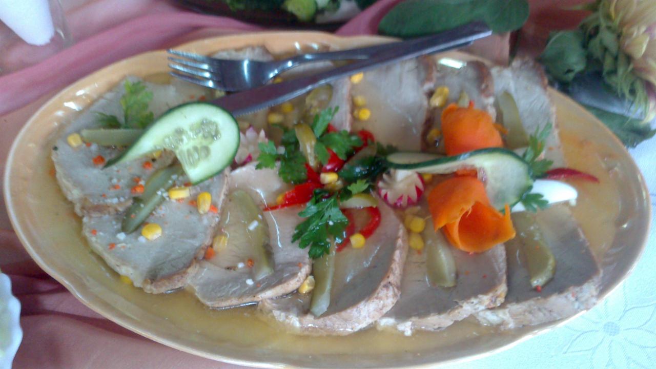 Półmisek z plastrami mięsa w galarecie, udekorowany ogórkiem, kukurydzą, papryką i natką pietruszki, z widelcem i nożem na wierzchu