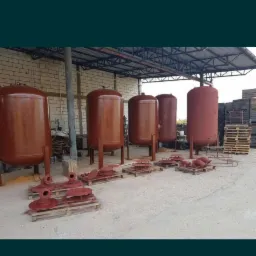 Cylindryczne zbiorniki metalowe po malowaniu proszkowym, ustawione na zewnątrz budynku, z elementami do montażu na paletach.