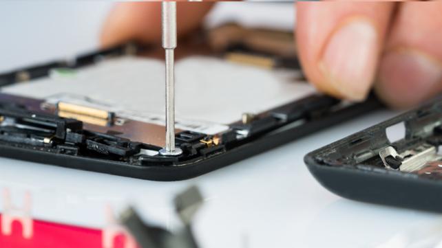 Odkręcanie małej śrubki w obudowie rozłożonego smartfona za pomocą precyzyjnego śrubokręta, widoczna metalowa konstrukcja i elementy elektroniki.