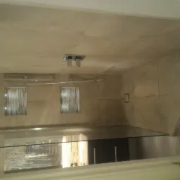 Wykończona łazienka z beżowymi płytkami, szklaną kabiną prysznicową i dekoracyjnym oświetleniem ściennym z trzema punktami świetlnymi.