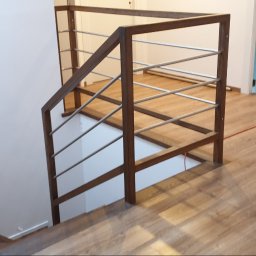 EBM Stolarstwo Tradycyjne - Nowoczesna balustrada schodowa z ciemnego drewna i metalowych prętów, widok z góry na drewnianą podłogę i białe ściany.