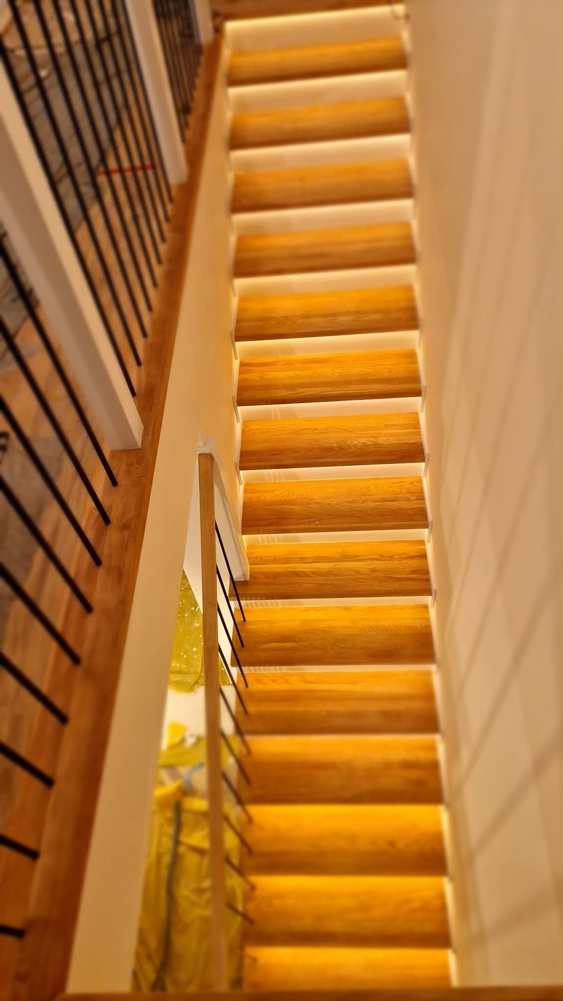 Drewniane schody z podświetleniem LED na każdym stopniu, czarne metalowe balustrady, widok z góry.