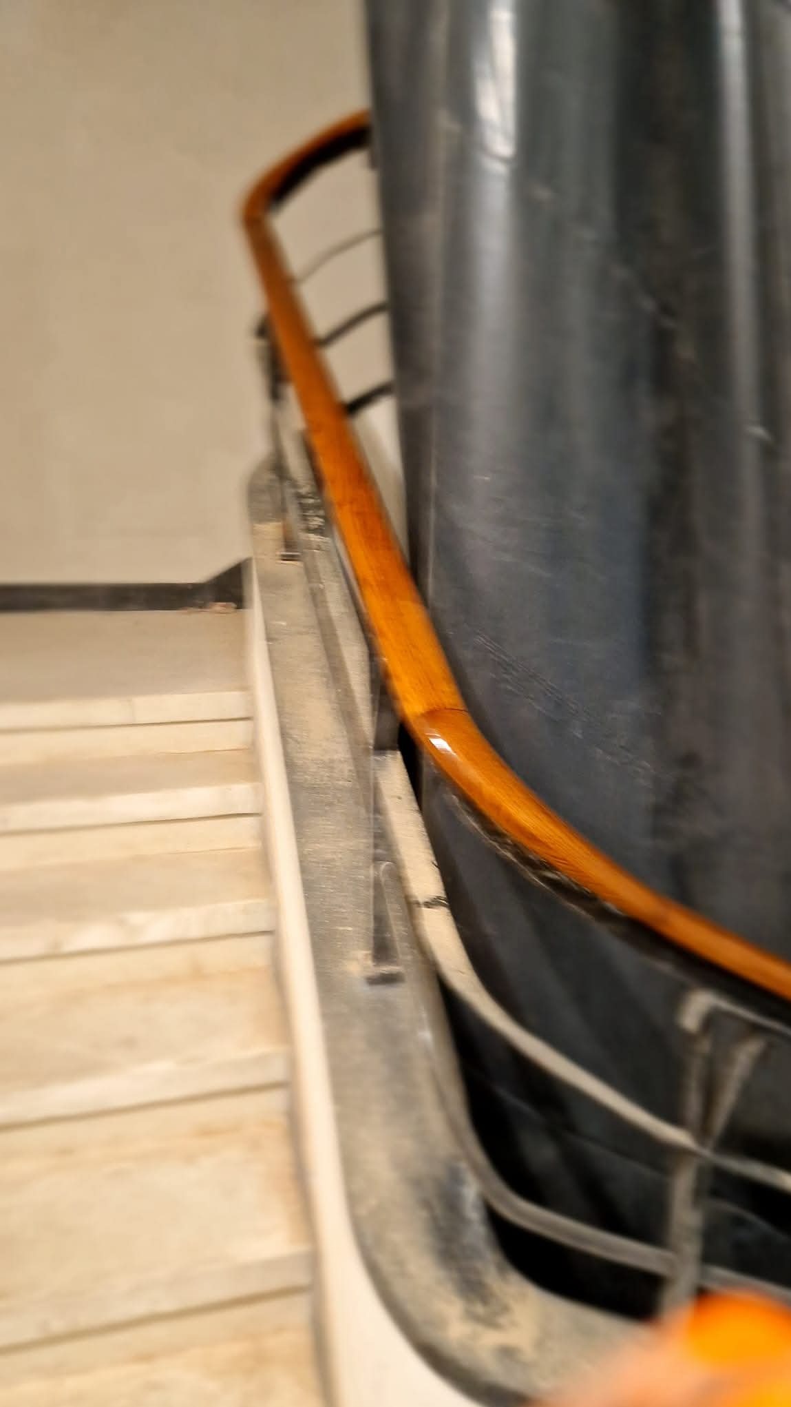 Fragment betonowych schodów z drewnianą poręczą o ciepłym odcieniu, zamontowaną na metalowej konstrukcji, widocznej z bliska pod kątem.