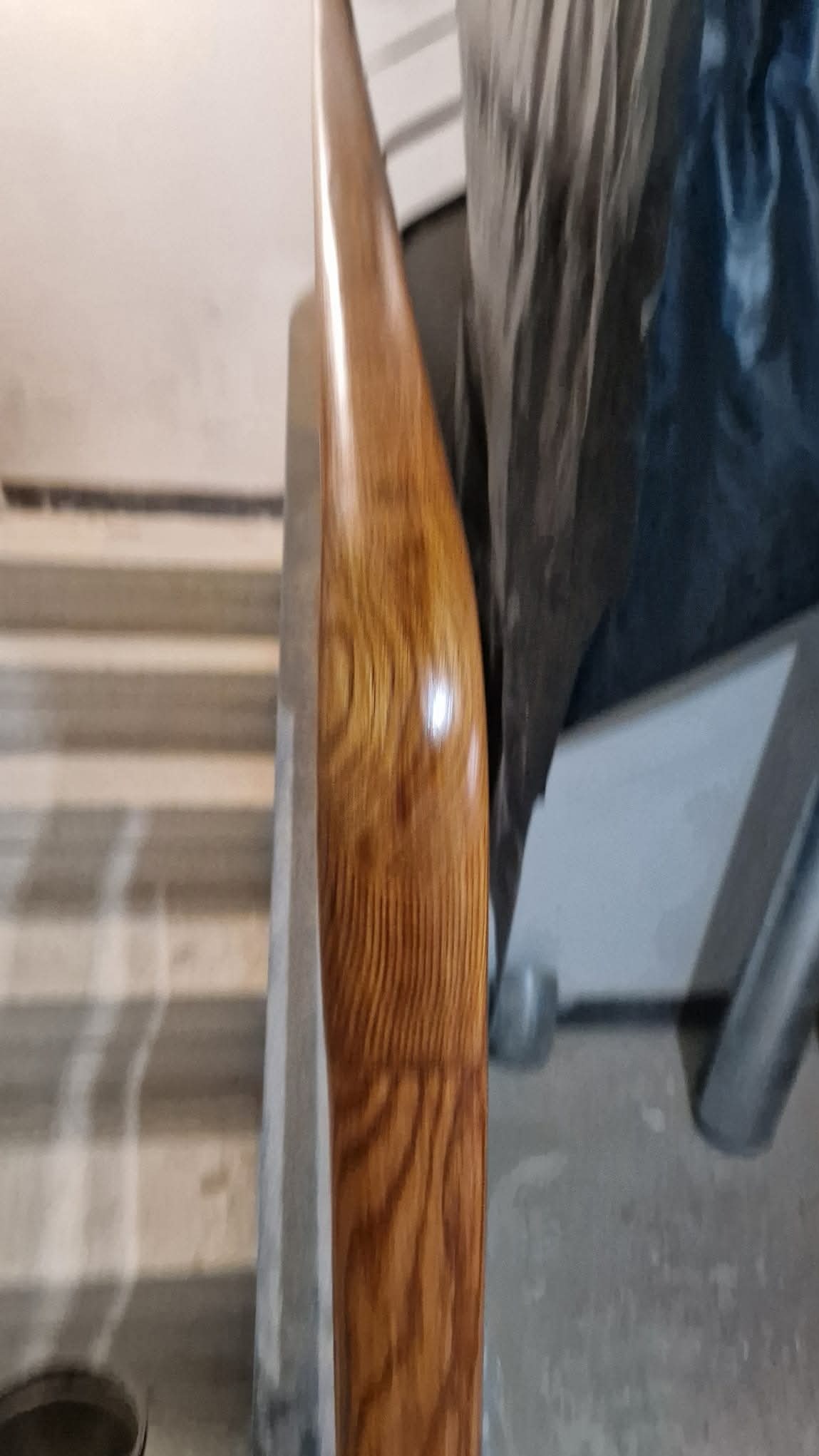 Polerowana drewniana poręcz schodowa z widocznym usłojeniem, zamontowana przy schodach z szarego betonu, częściowo zakryta materiałem ochronnym.