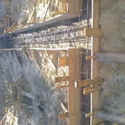 Szczegółowe ujęcie szalunku i zbrojenia fundamentu w wykopie, przygotowanego do zalania betonem, z widocznymi drewnianymi elementami konstrukcyjnymi i stalowymi prętami zbrojeniowymi.