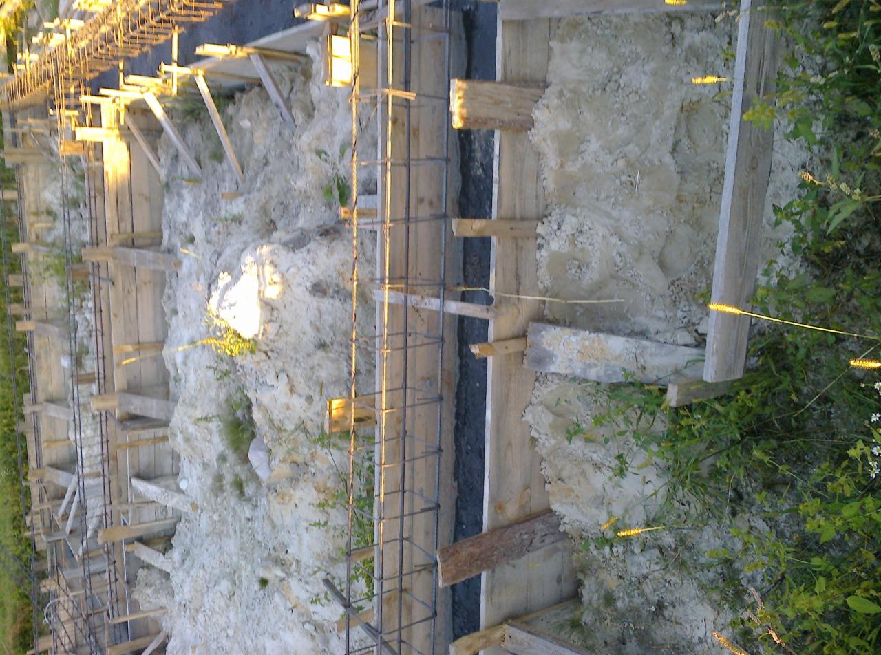 Wykop z drewnianym szalunkiem i zbrojeniem stalowym przygotowany do zalania betonem pod fundament budynku, widok z góry.