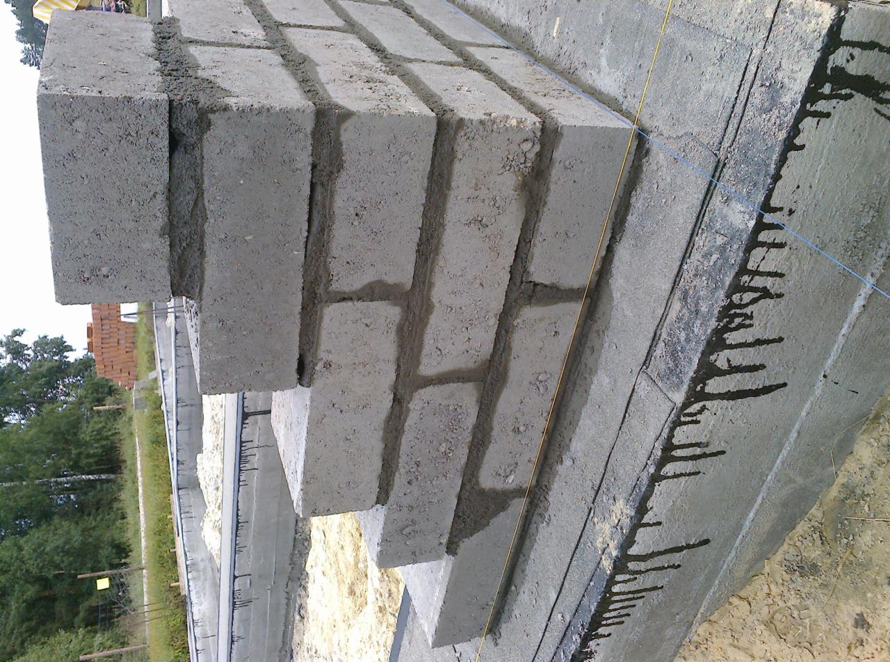 Wznoszenie ściany fundamentowej z bloczków betonowych, widoczne świeże ślady zaprawy i poziomica sznurkowa.