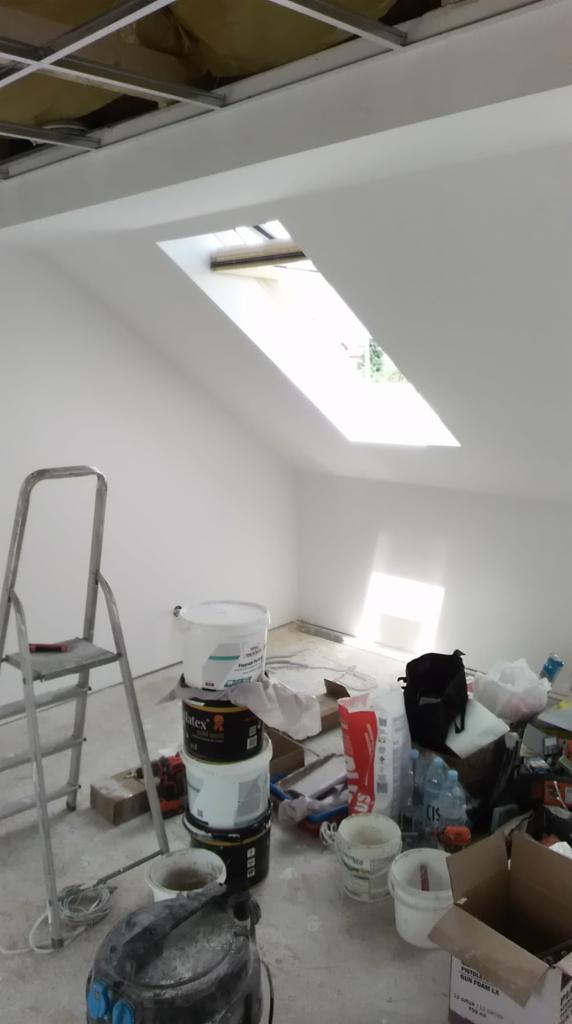 Pokój na poddaszu w Hecznarowicach w trakcie malowania na biało, widoczne okno dachowe, drabina, puszki z farbą i inne akcesoria malarskie.
