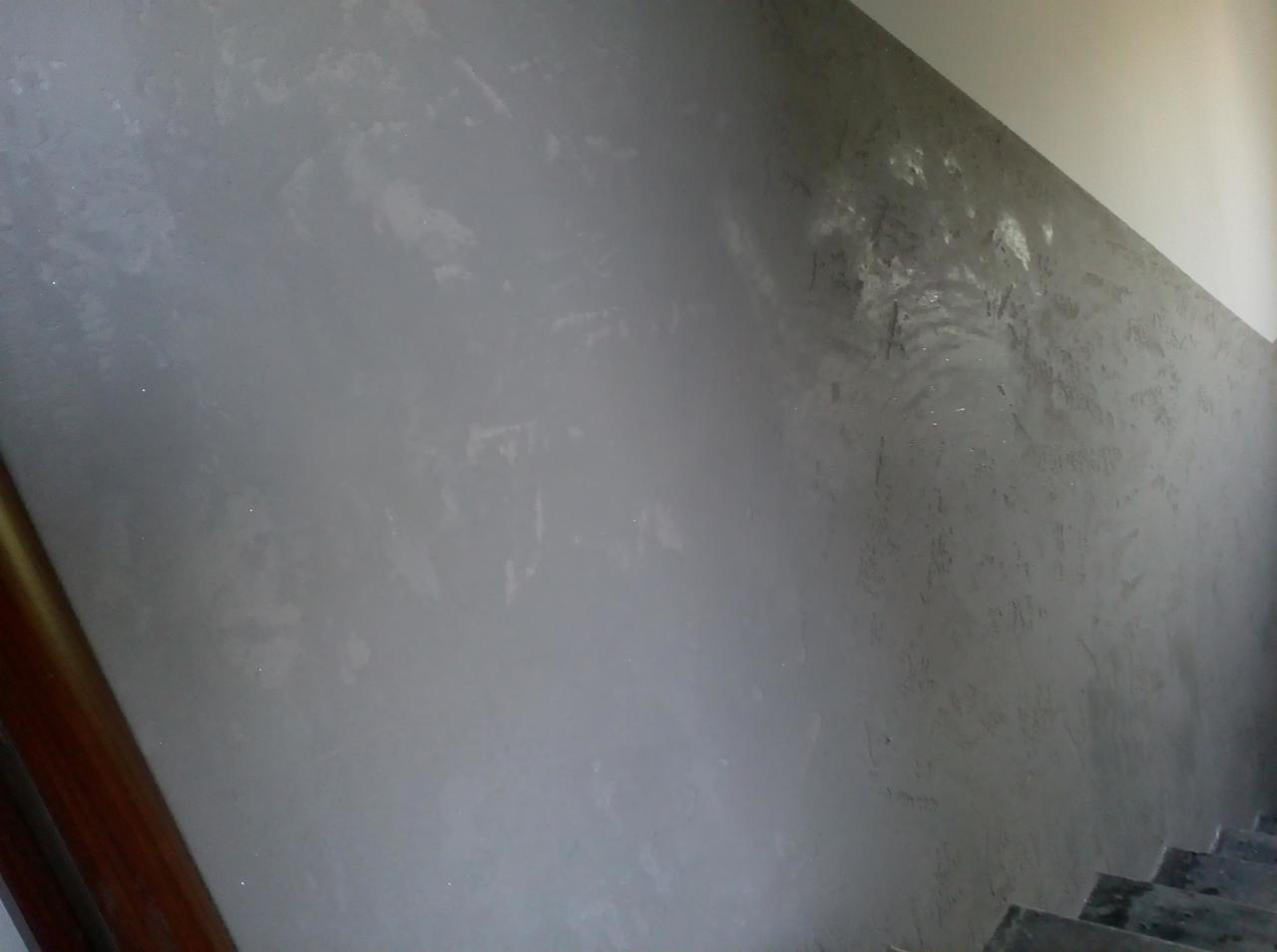 Szara ściana z dekoracyjną fakturą w korytarzu, widoczne schody z szarego kamienia i fragment brązowej ramy drzwi.