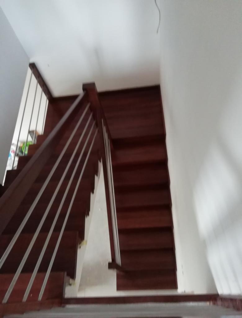 Widok z góry na ciemne, drewniane schody z metalowymi poręczami w jasnym wnętrzu, z widocznym kablem zwisającym z sufitu.