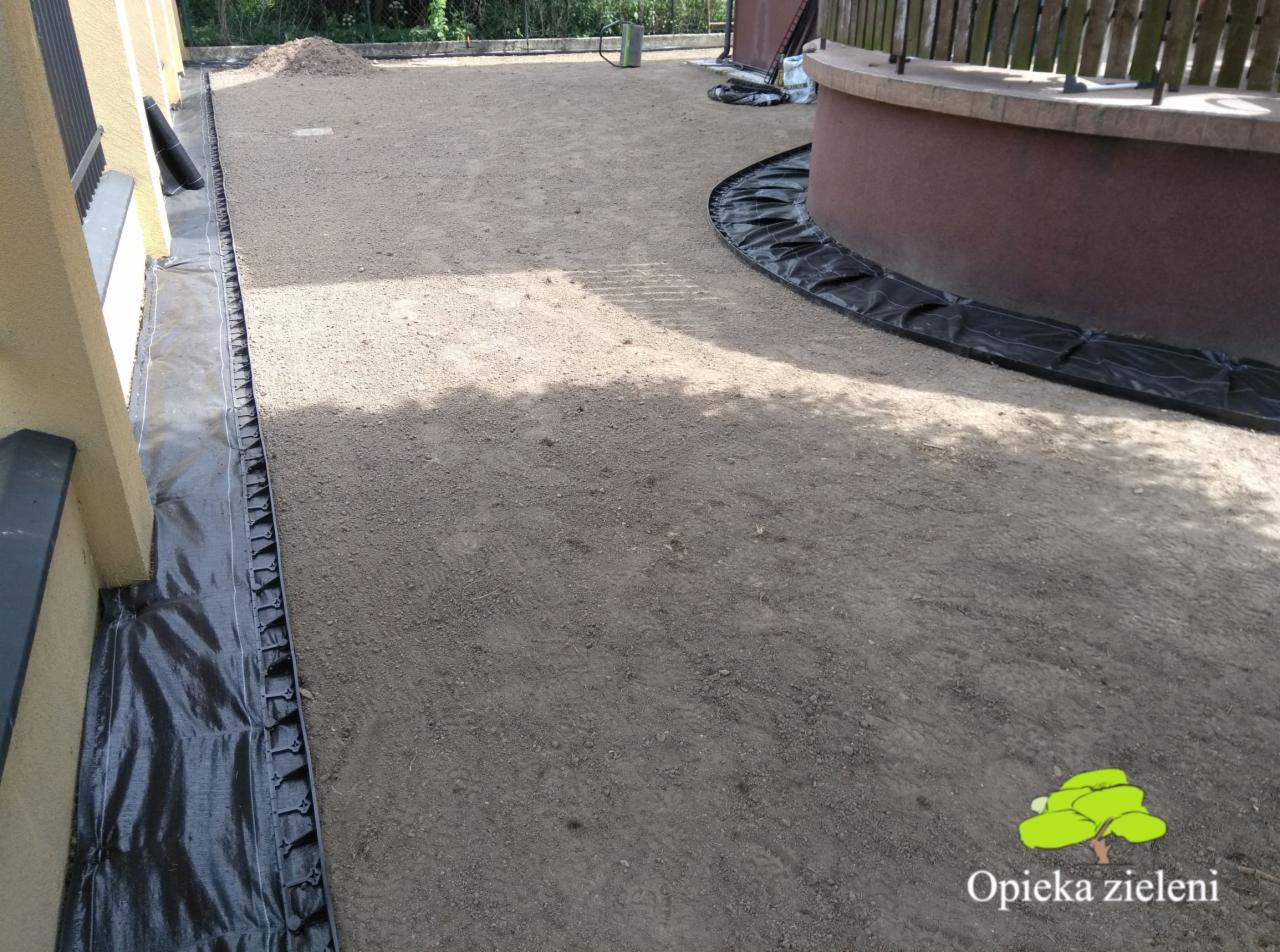 Przygotowanie podłoża pod trawnik z rolki: wyrównana ziemia, obrzeża z czarnej folii, widoczny budynek i fragment tarasu.