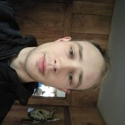 Rsinformatyka - Portret młodego mężczyzny w czarnej kurtce na tle drewnianej ściany. Ujęcie z bliska, z lekkim uśmiechem.