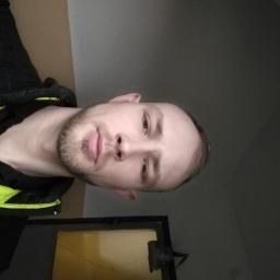 Rsinformatyka - Portret mężczyzny z brodą, ubranego w kurtkę z neonowymi elementami, w pomieszczeniu z oknem. Nietypowy kadr z dołu.