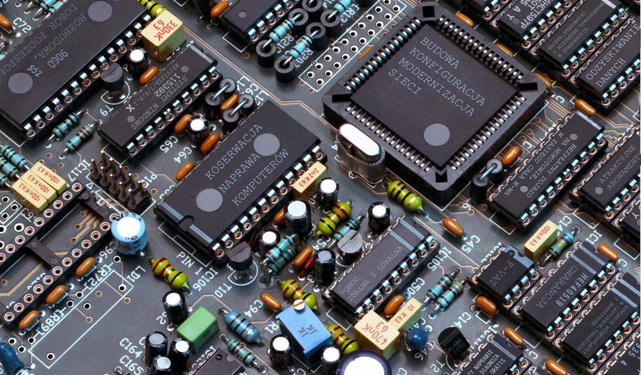 Zbliżenie na płytę główną komputera z widocznymi układami scalonymi, kondensatorami, rezystorami i innymi elementami elektronicznymi, prezentujące skomplikowaną budowę wewnętrzną urządzenia.