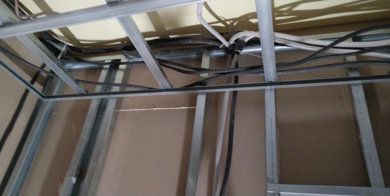 Metalowa konstrukcja sufitu podwieszanego z widocznymi przewodami elektrycznymi i kablami, zamocowanymi do stropu.