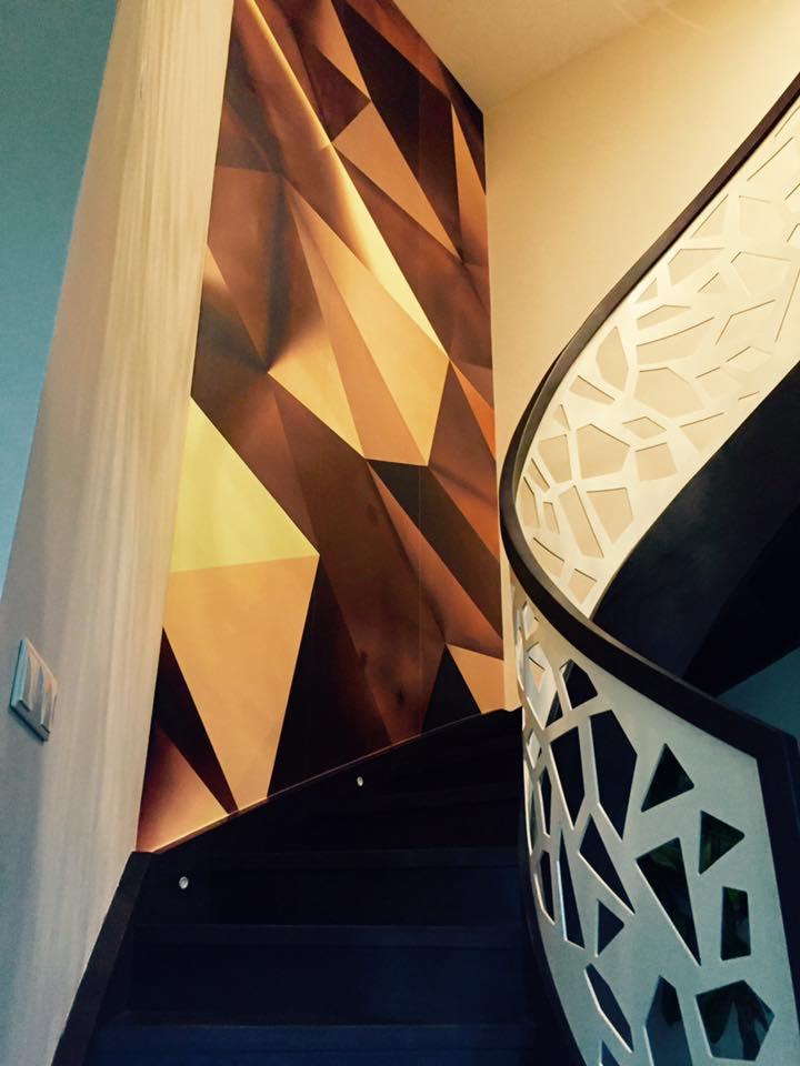 Tapeta z geometrycznym wzorem w odcieniach brązu i złota na ścianie przy schodach z ażurową balustradą w nowoczesnym wnętrzu.