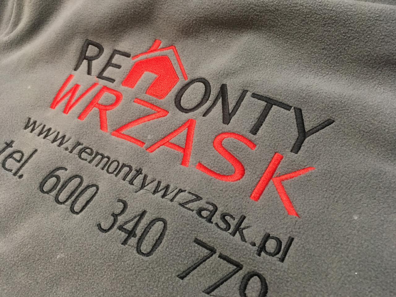 Szara bluza polarowa z wyhaftowanym logo firmy remontowej 'REMONTY WRZASK', zawierającym czerwony symbol domu i dane kontaktowe: adres strony internetowej oraz numer telefonu.