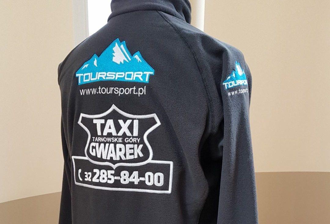 Czarna bluza polarowa z wyhaftowanymi logo firm: Toursport (góry, nazwa, adres strony) oraz Taxi Tarnowskie Góry Gwarek z numerem telefonu, widok z tyłu.