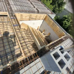 Wiązanie zbrojenia stropu na drewnianym szalunku, widoczny cień osoby robiącej zdjęcie, bloczki betonowe i elementy murowane.