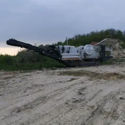 Duża, gąsienicowa maszyna do kruszenia kamienia marki Lokotrack LT116, stojąca na placu budowy w Łaziskach Górnych, z widocznym fragmentem czerwonej naczepy i śladami opon na ubitej ziemi.