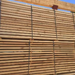 Stos tarcicy budowlanej związany taśmami, widoczne niebo i pole w tle.