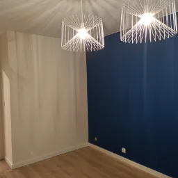 Pomalowane na biało i granatowo ściany w pustym pokoju z drewnianą podłogą, oświetlonym dwoma nowoczesnymi, białymi lampami wiszącymi.