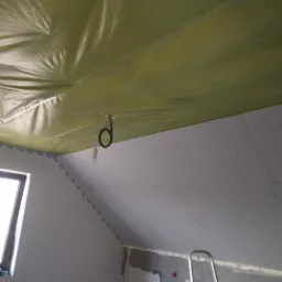 Poddasze w trakcie wykańczania: folia paroizolacyjna na suficie, płyty gipsowo-kartonowe na ścianach, widoczne przewody elektryczne i drabina.