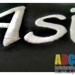 Biały, wypukły napis 'Asi' wykonany na czarnej tkaninie, w prawym dolnym rogu logo firmy hafciarskiej 'ABC hafciarnia Kamil Kowalczyk'.