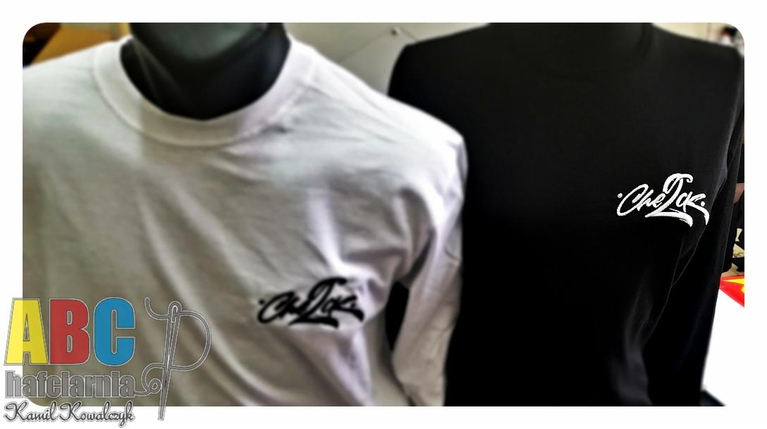 Dwie koszulki na manekinach: biała i czarna, z identycznym białym napisem 'Che Ink' w lewym górnym rogu. Na pierwszym planie widoczne logo firmy 'ABC hafciarnia Kamil Kowalczyk'.