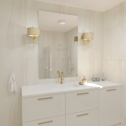 BOHO STUDIO - Elegancka łazienka z białymi szafkami pod umywalką, złotą armaturą i marmurowymi ścianami, oświetlona kinkietami z abażurami w kolorze beżowym.