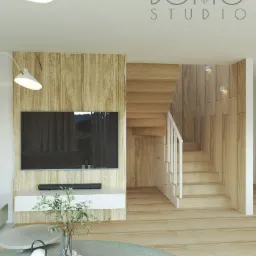 Wizualizacja salonu z drewnianymi schodami, telewizorem na ścianie z okładziną imitującą drewno, okrągłym stolikiem kawowym z wazonem i lampką oraz logotypem 'BOHO STUDIO' w górnym rogu.
