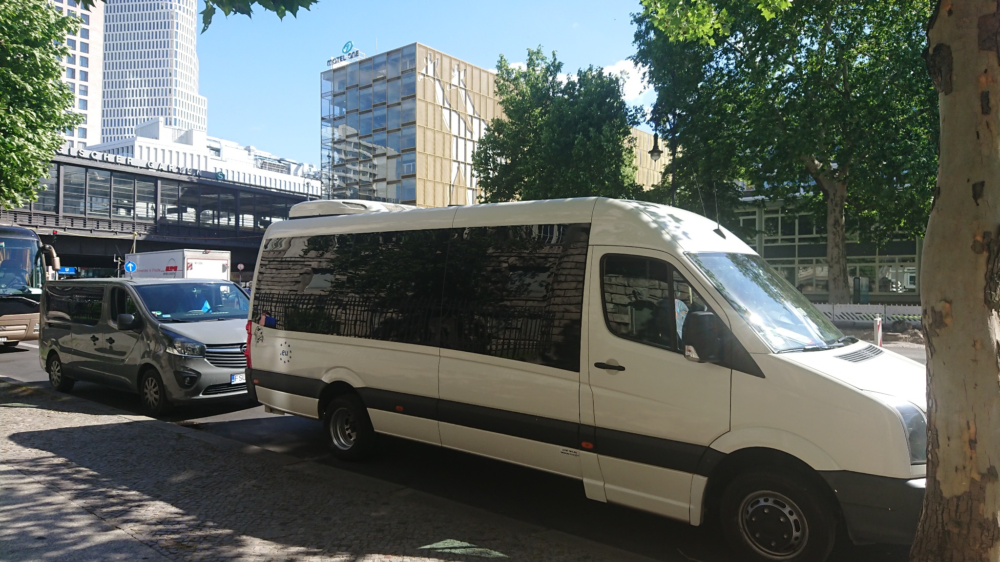 Biały bus pasażerski zaparkowany na ulicy w Berlinie, w tle widoczne budynki z charakterystyczną architekturą.
