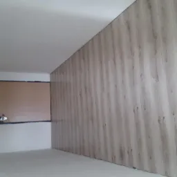 Ściana wykończona panelami imitującymi drewno, widoczne niedoskonałości szpachlowania na sąsiedniej ścianie przygotowanej do dalszych prac wykończeniowych.