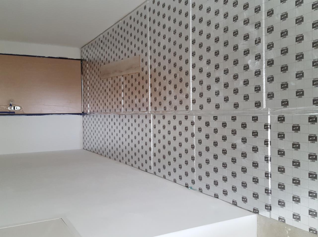 Przygotowane ściany do prac wykończeniowych, zabezpieczone folią malarską i taśmą, widoczny fragment sufitu i podłogi w trakcie remontu.