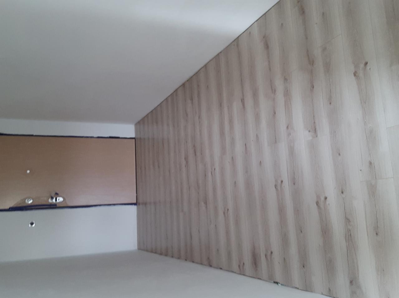 Ściana wykończona panelami imitującymi drewno, widoczne niedoskonałości szpachlowania na sąsiedniej ścianie przygotowanej do dalszych prac wykończeniowych.