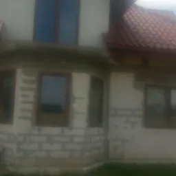 Dom jednorodzinny w trakcie ocieplania elewacji, widoczne bloczki i częściowo nałożony klej, brązowe ramy okienne, dach z czerwonej dachówki, tabliczka z numerem posesji 33A.