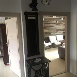 Wnętrze z odrestaurowaną podłogą z desek, ścianą z drewnianych paneli i dekoracyjnym stolikiem ze starej maszyny do szycia.