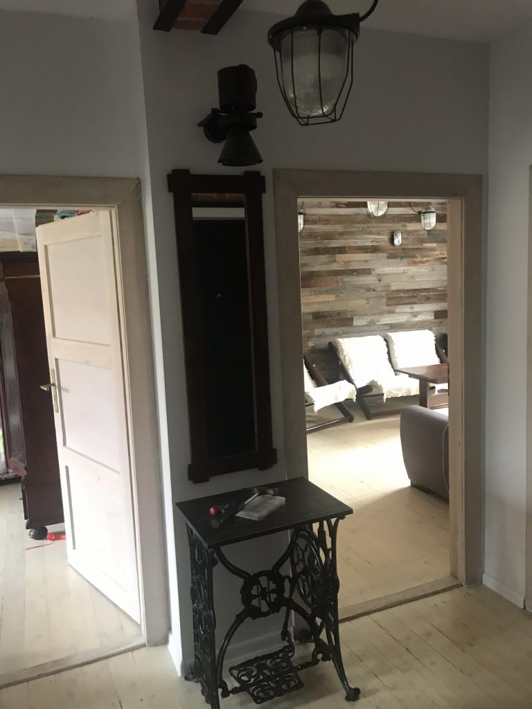 Wnętrze z odrestaurowaną podłogą z desek, ścianą z drewnianych paneli i dekoracyjnym stolikiem ze starej maszyny do szycia.