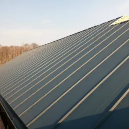 Nowe pokrycie dachowe z blachy na dachu domu jednorodzinnego, widoczne obróbki blacharskie i fragment rusztowania w tle.