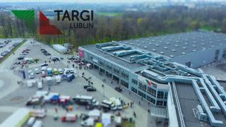 Panorama Targów Lublin z lotu ptaka, widoczny budynek hali wystawienniczej z parkingiem pełnym samochodów i zielenią w tle.