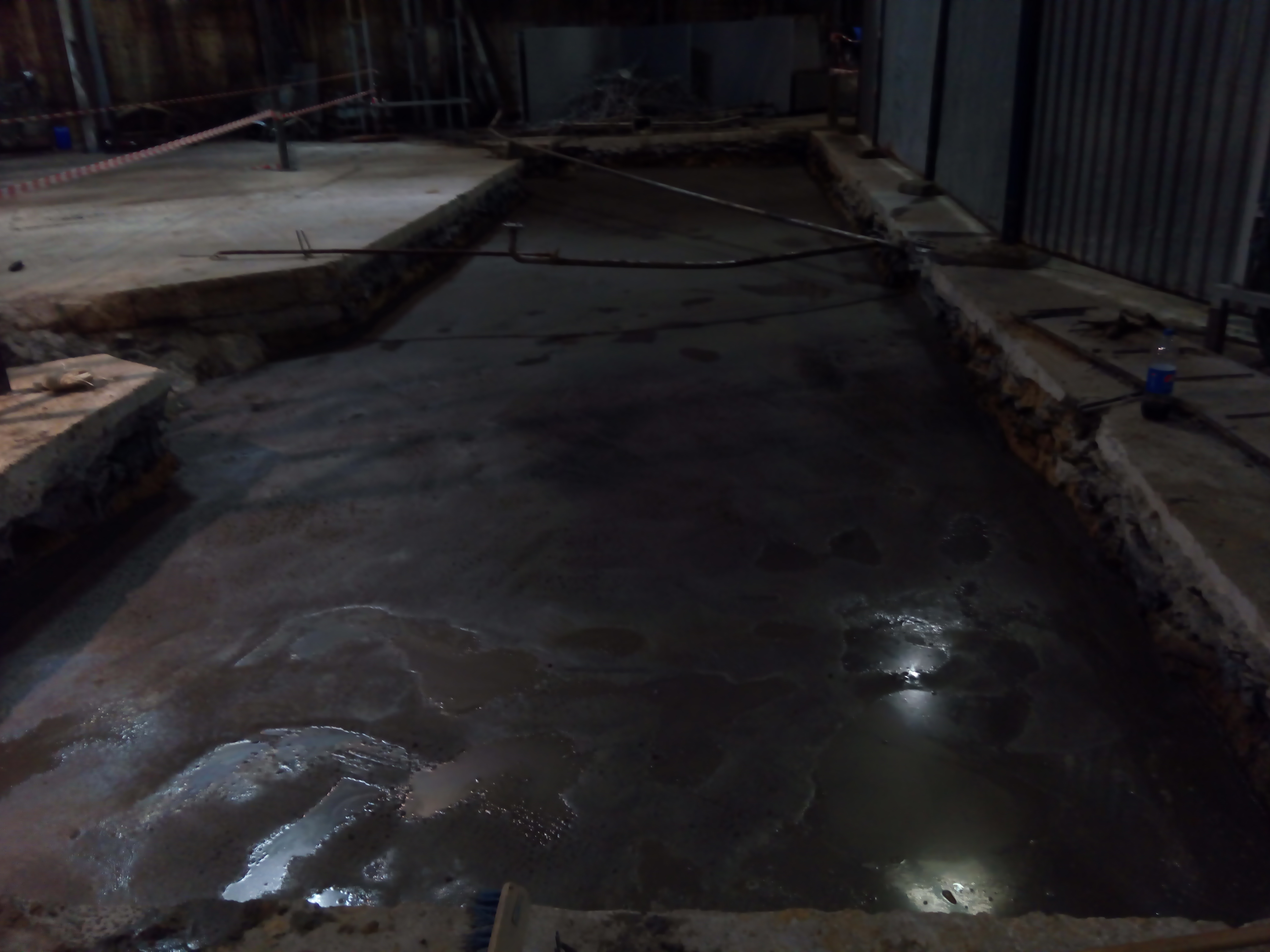 Świeżo wylana, ciemna wylewka betonowa w przygotowanych szalunkach fundamentowych, widoczne kable i rurki wystające z betonu.