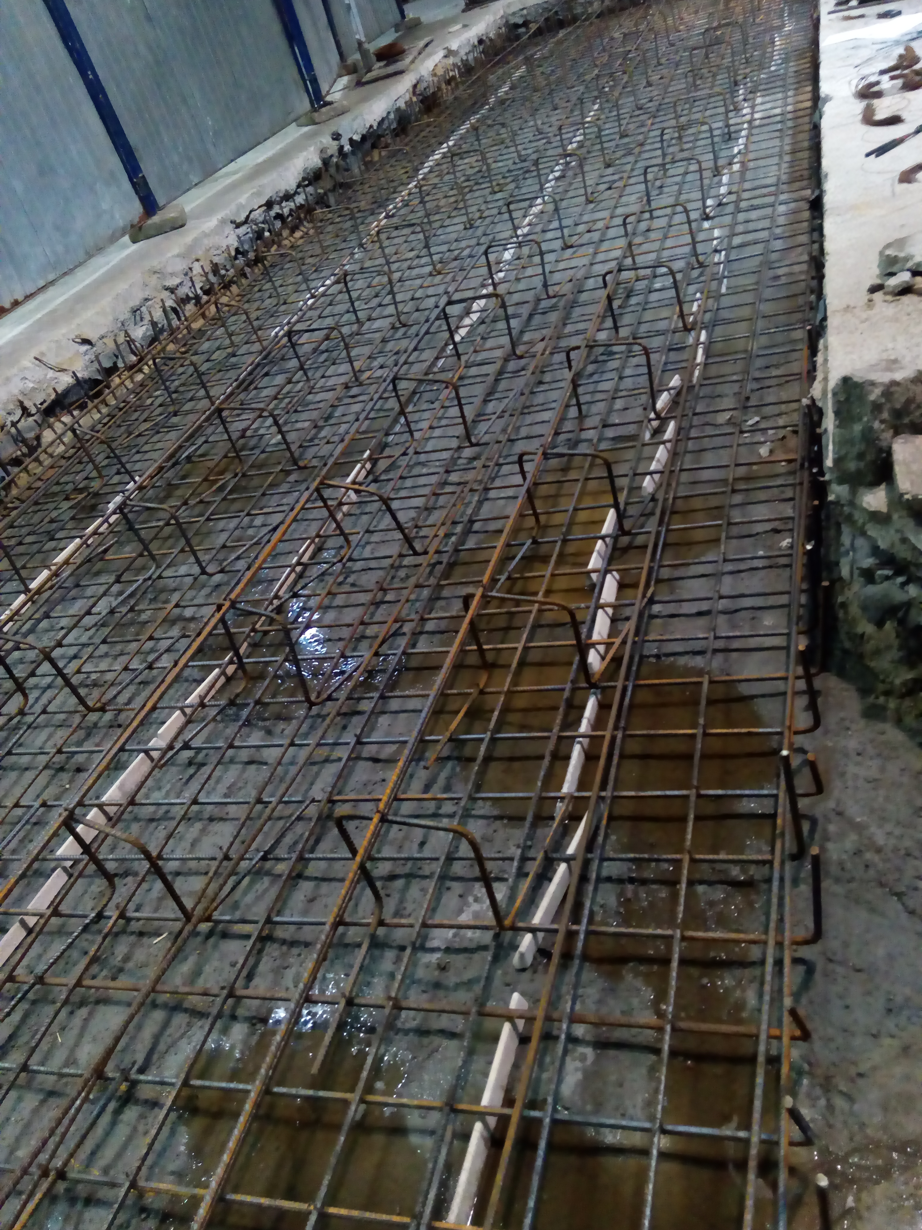 Siatka zbrojeniowa z dystansami ułożona na mokrej powierzchni, przygotowana do zalania betonem.