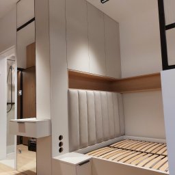 Zbigniew Czerech - Nowoczesna zabudowa sypialni z łóżkiem i szafami w jasnej kolorystyce. Uwagę zwraca tapicerowane wezgłowie i lustrzane elementy. Minimalistyczny design.