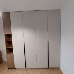 Zbigniew Czerech - Duża, nowoczesna szafa wnękowa z beżowymi frontami i drewnianymi elementami, dopasowana do wnętrza. Cztery pionowe, czarne uchwyty. Parkiet w jodełkę.